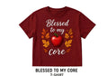 A short-sleeve crewneck t-shirt in maroon red, featuring a graphic print with the text 'Blessed to my core' in white script, a red apple in the center, and orange and yellow autumn leaves. The image is presented on a light background with black side bars and text overlays indicating size and product type.