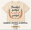A natural beige short-sleeve t-shirt with a graphic print that reads 'Thankful, faithful and grateful' in black and orange lettering, framed by an orange leaf wreath and small hearts. Below the shirt, text reads 'THANKFUL, FAITHFUL & GRATEFUL T-SHIRT', 'NATURAL', and 'S - 5XL'.